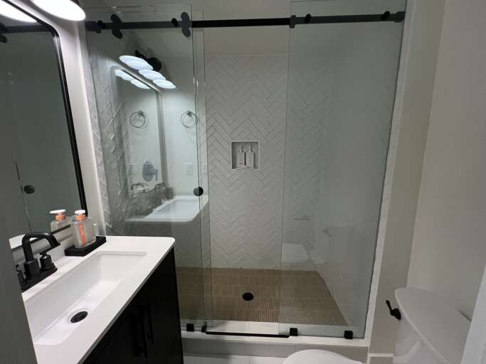 One of two bathrooms with a single vanity and an oversized custom shower. One bathroom is ensuite with a bedroom and the other is open to the hallway.
