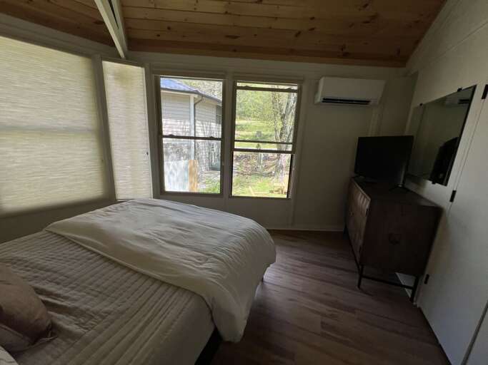 One of two Queen bedrooms with mini split for AC, a ceiling fan, windows with shades, and a TV