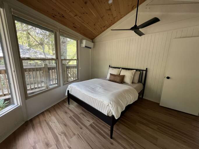 One of two Queen bedrooms with mini split for AC, a ceiling fan, windows with shades, and a TV
