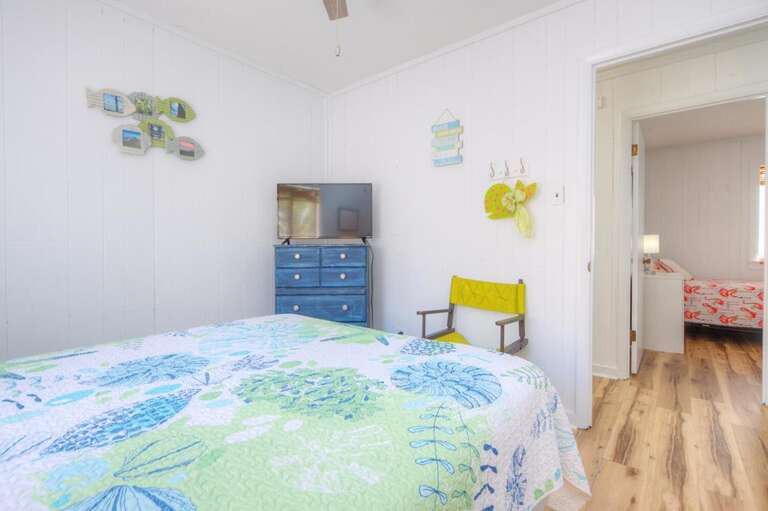 Bright Bedroom With Floral Quilt, Blue Dresser, And Wooden Floor