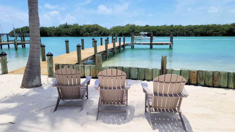 Chairs On Beach Facing A Dock And Turquoise Water
