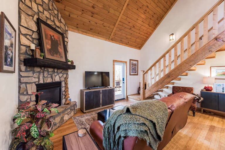 Rustic Living Room With Stone Fireplace, Wooden Beams, Staircase, And Television