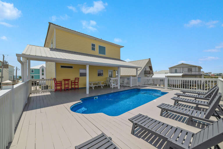 Yellow House With Pool, Patio, And Deck Chairs Under Blue Sky