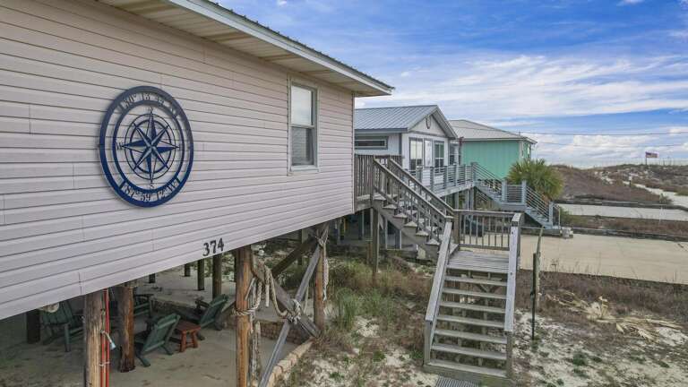 Stilted Seaside Structure Sporting A Nautical Symbol, Steps Sweep Up To Sandy Stretch