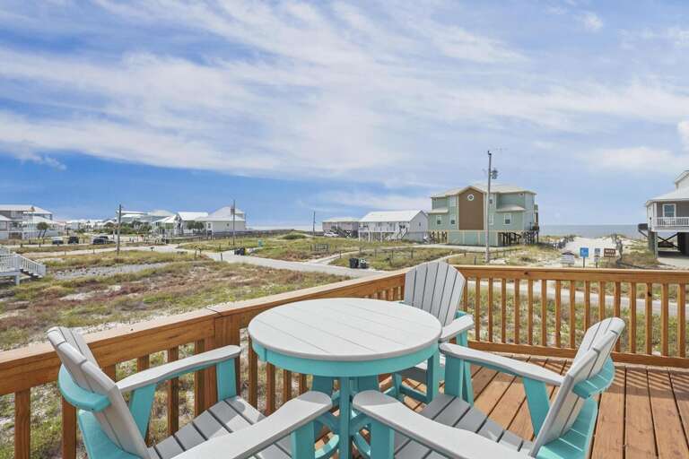 Seaside Structure Showing Elevated Deck With Turquoise Table, Chairs Overlooking Beach