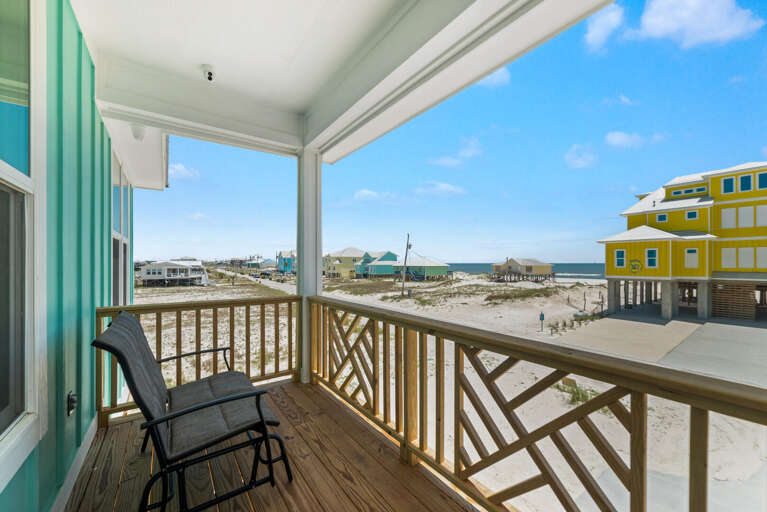 Balcony View Of Beachfront, Featuring Chair And Railing, Overlooking Sandy Dunes And Distant Buildings