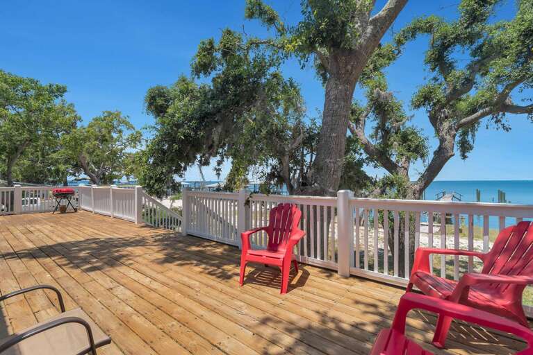 Seaside Deck With Red Chairs, Railing, And Tree Shade
