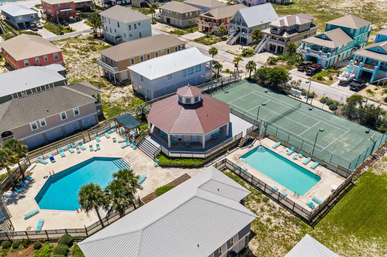 Aerial View Of Circular Building Surrounded By Pools And Tennis Courts Next To Several Houses