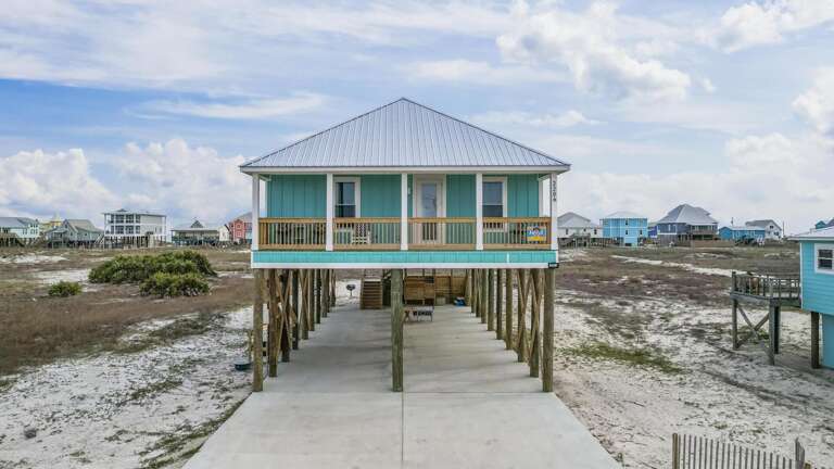 Beachfront Building Beneath Blue Skies, Balancing On Stilts Above Sandy Shore