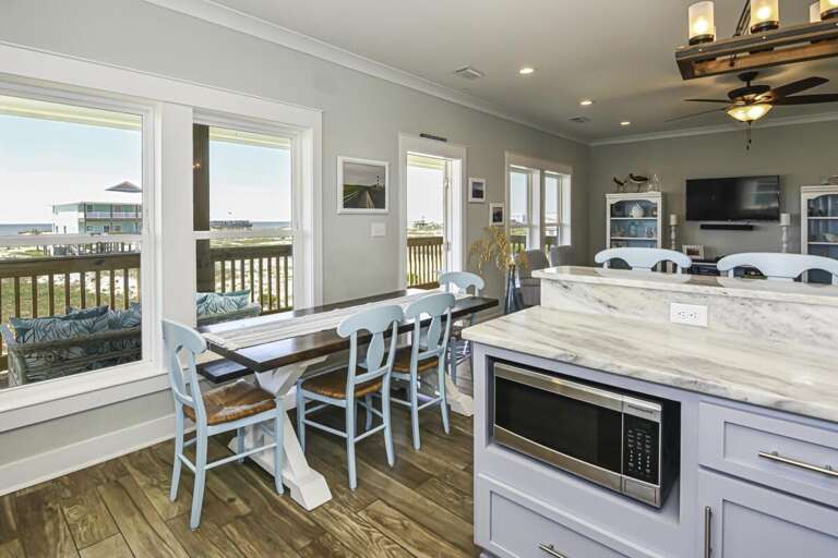 Bright Beachside Kitchen With Blue Bar Stools, White Cabinetry, And A Scenic Window View