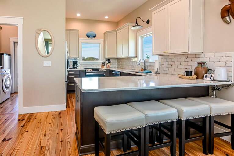 Spacious Kitchen With Sleek Surfaces, Shining Stools, And Soft Sunlight Streaming Through