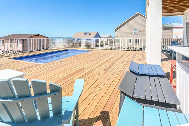 Spacious Deck With Pool And Chairs Under Sunny Skies Near Beachfront Vacation Rental