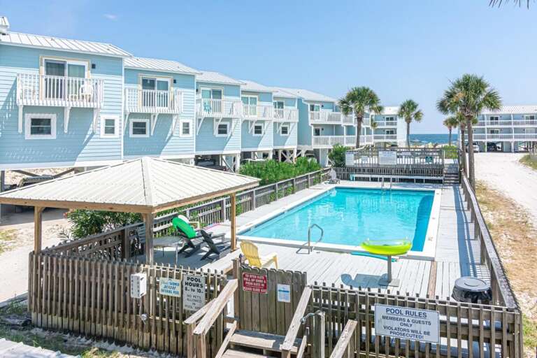 Blue Buildings Bordering A Bright Pool, Palms Peeking, Sunny Sky