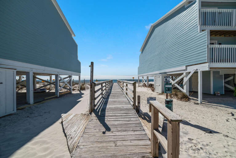 Wooden Walkway Winding Between Beachside Buildings Leading To Sandy Shore
