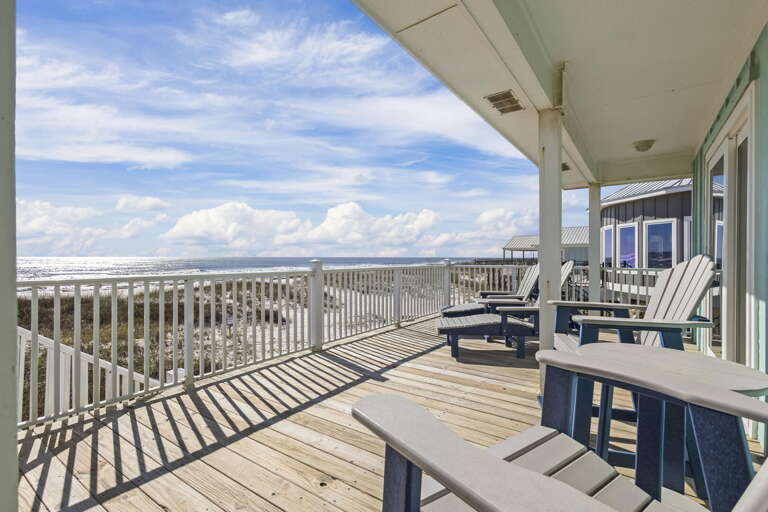 Seaside Deck Of A Beach-facing Vacation Rental With Chairs And Table, Under A Bright Sky