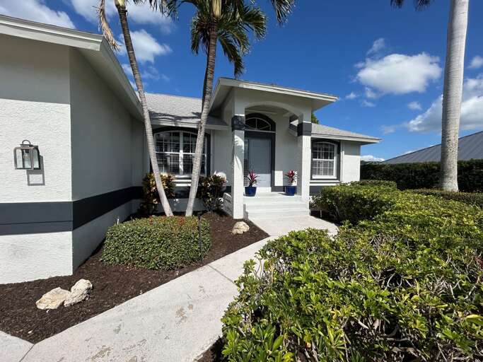 Vacation Rental: Palm-lined Pathway Leading To A Blue-doored Bungalow Under Bright Skies